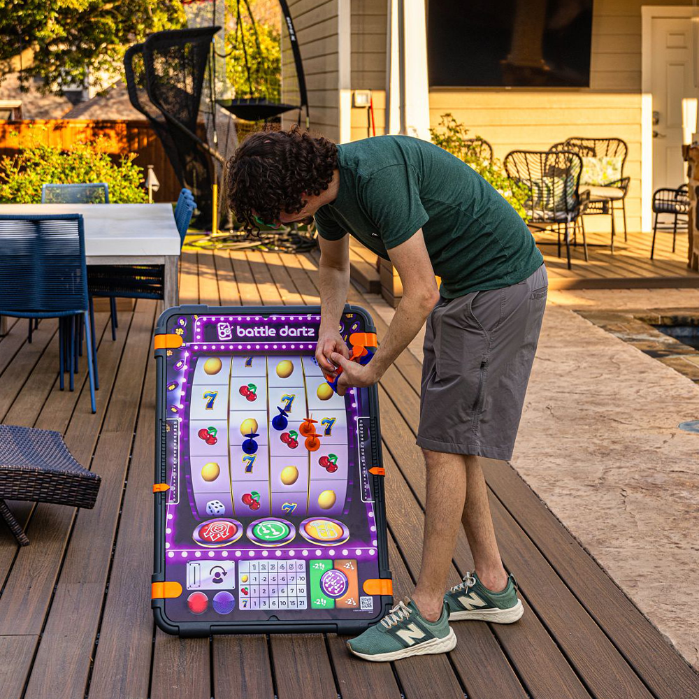 Person playing a game on an outdoor deck with a large screen displaying a game interface.